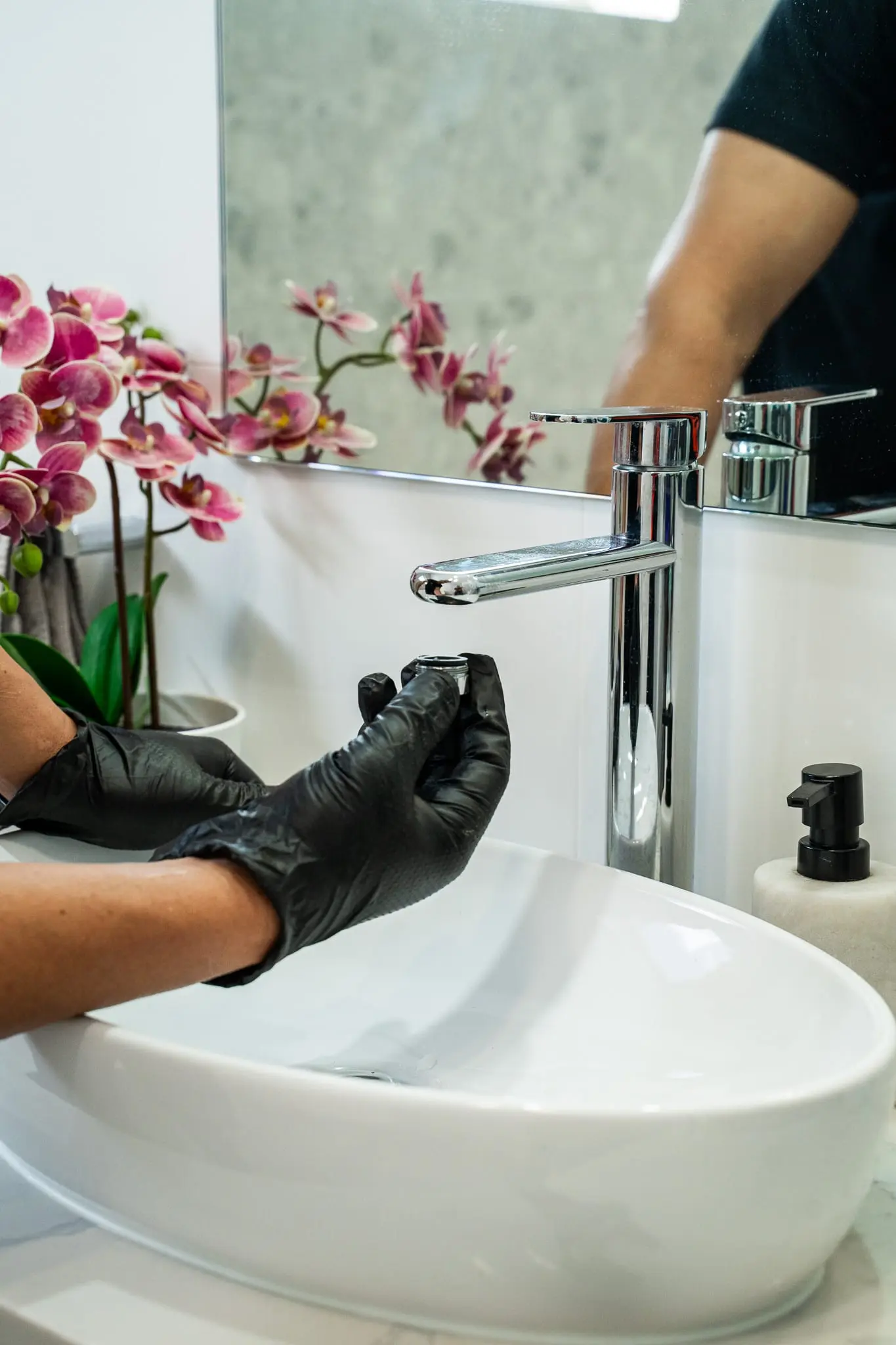 Close-up of gloved hands repairing a chrome basin mixer