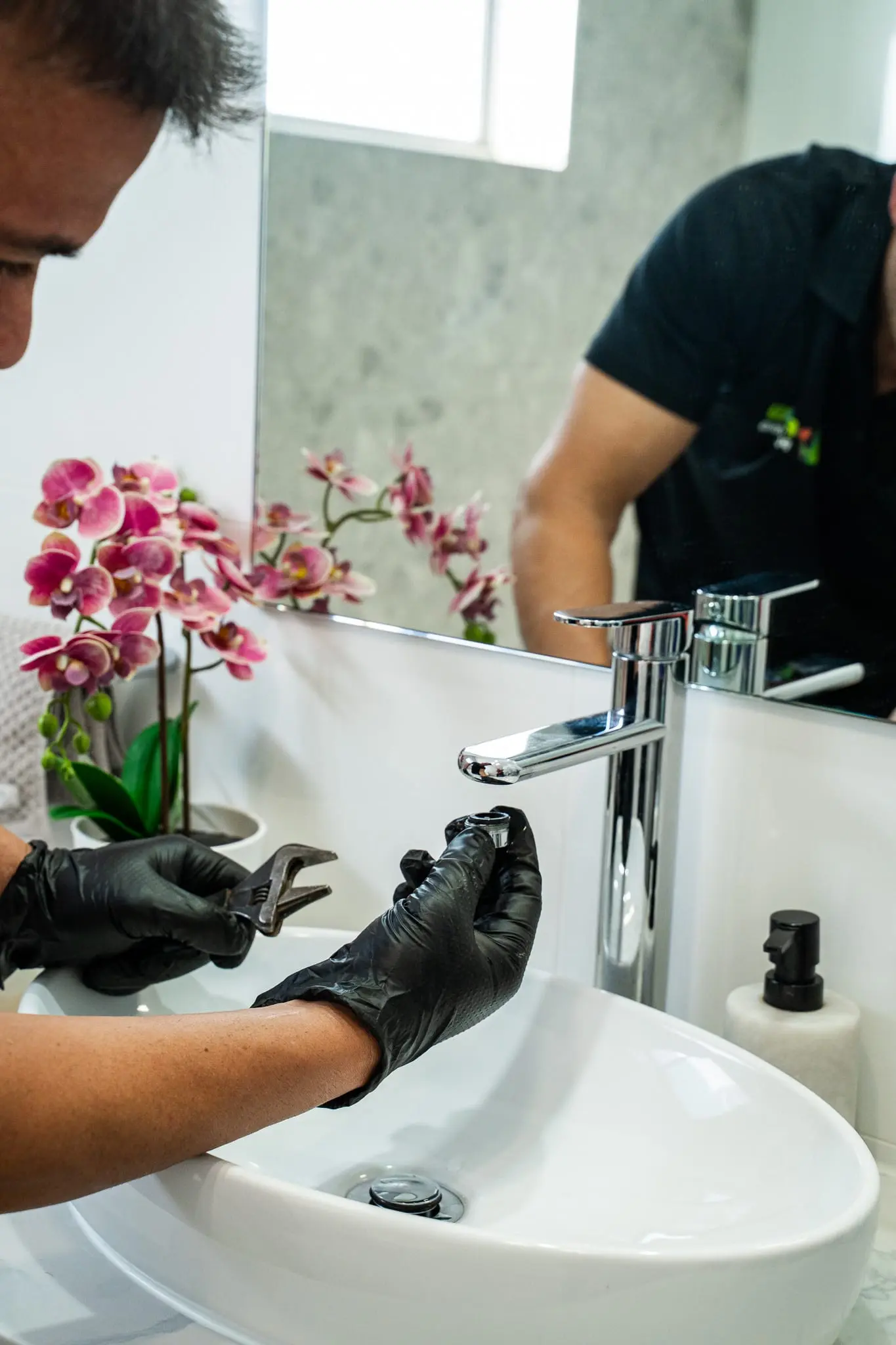 Plumber tightening a basin mixer tap, reflected in the bathroom mirror