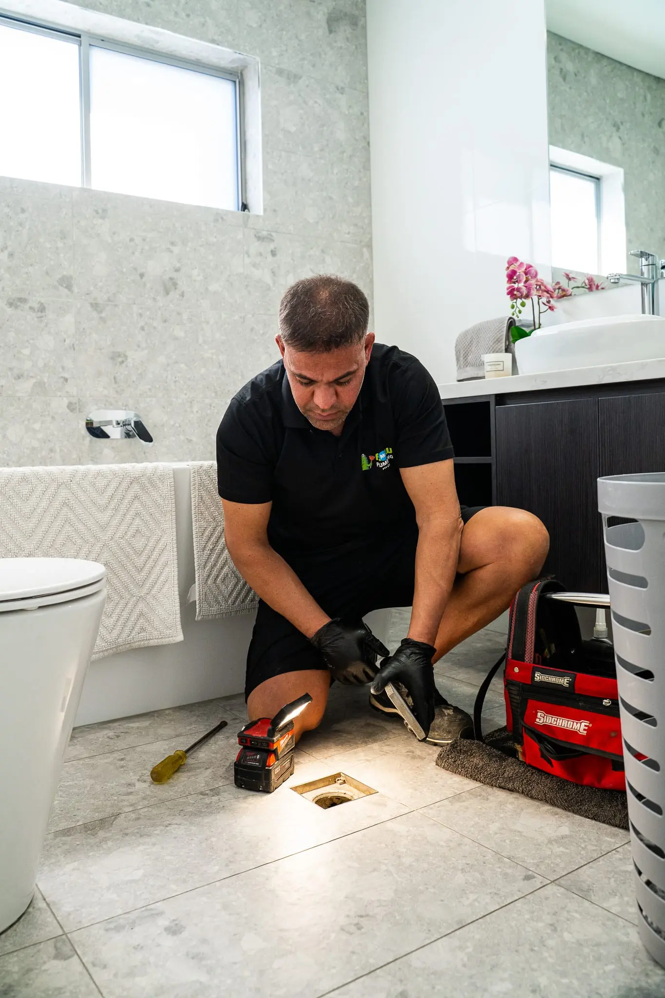 Mr Flow plumber inspecting a bathroom floor waste with a work light