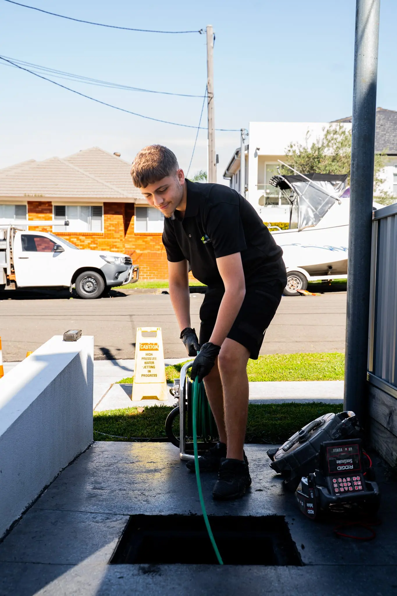 Plumber lowering a jet blaster hose into an outdoor drain pit