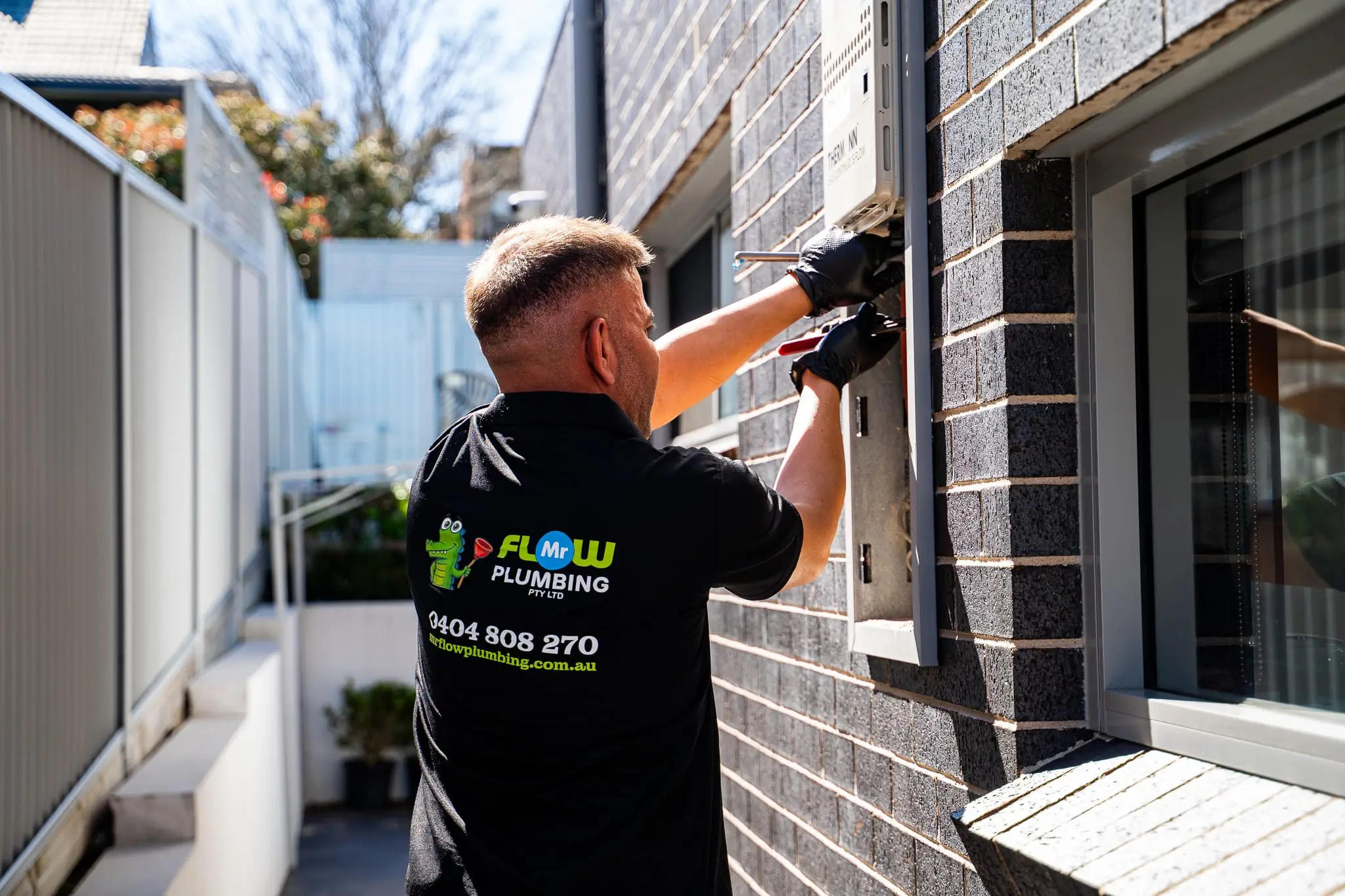 Mr Flow plumber repairing a gas continuous-flow hot water system on a brick wall