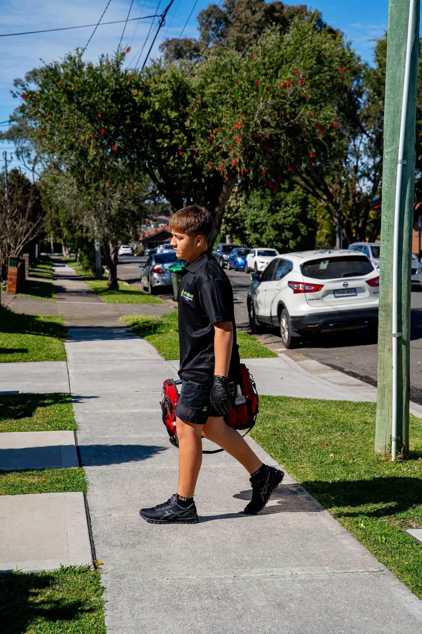 Mr Flow plumber walking to a job along a leafy Sydney footpath with his toolbag