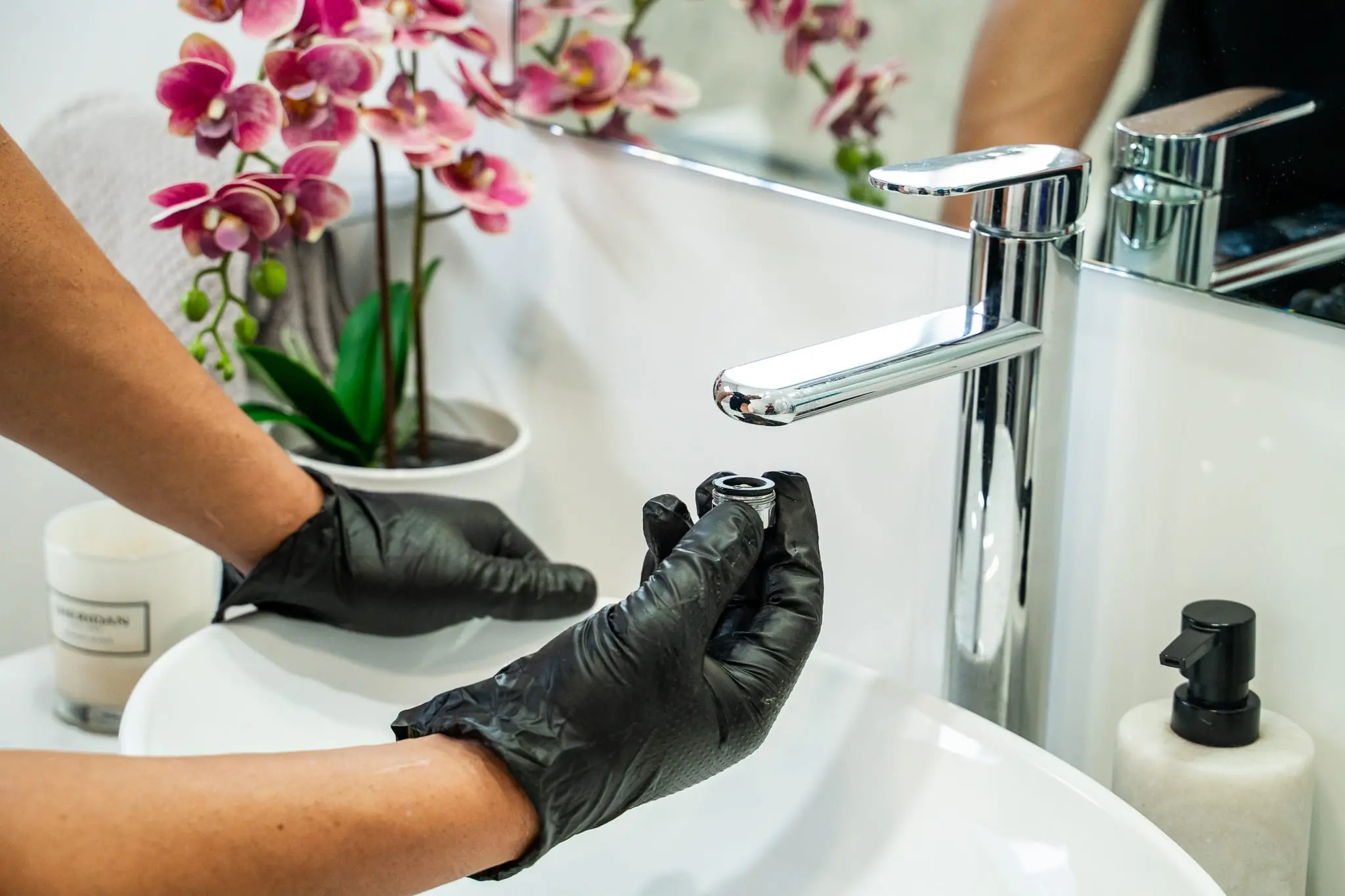 Gloved hands fitting a chrome basin mixer in a bathroom
