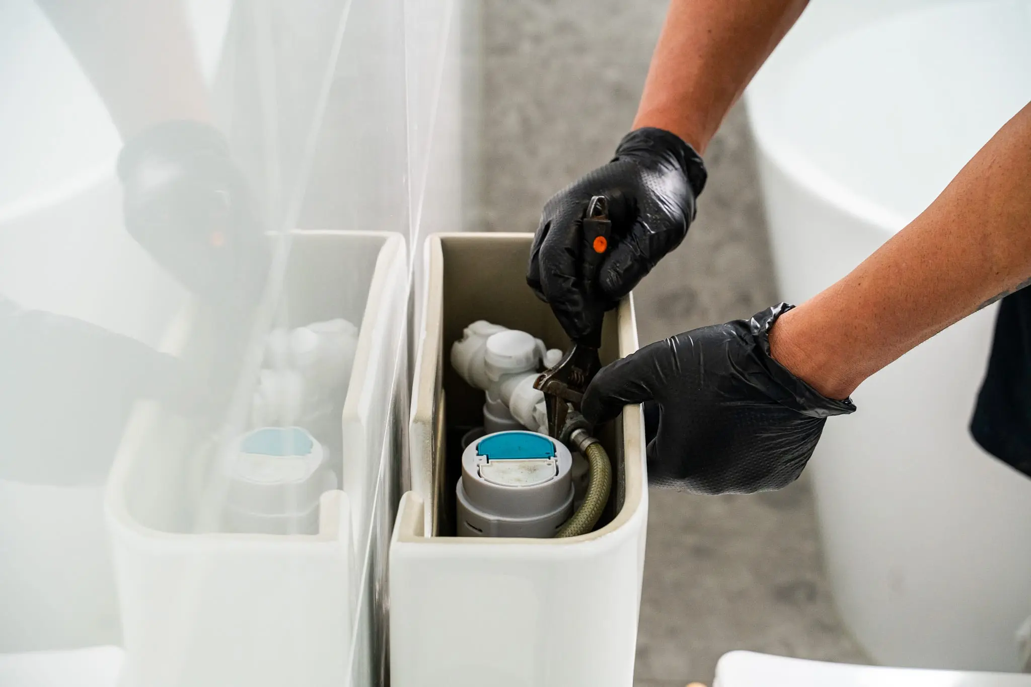 Close-up of gloved hands working on the valves inside a toilet cistern